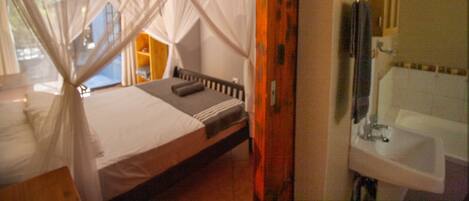 A room with a bed, a window with a view, a bathroom with a sink, and a mirror.