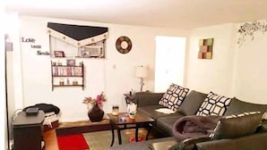 A living room with a sofa, a coffee table, a bookshelf, and a wall clock. - SmileVew Apartments (Accra)