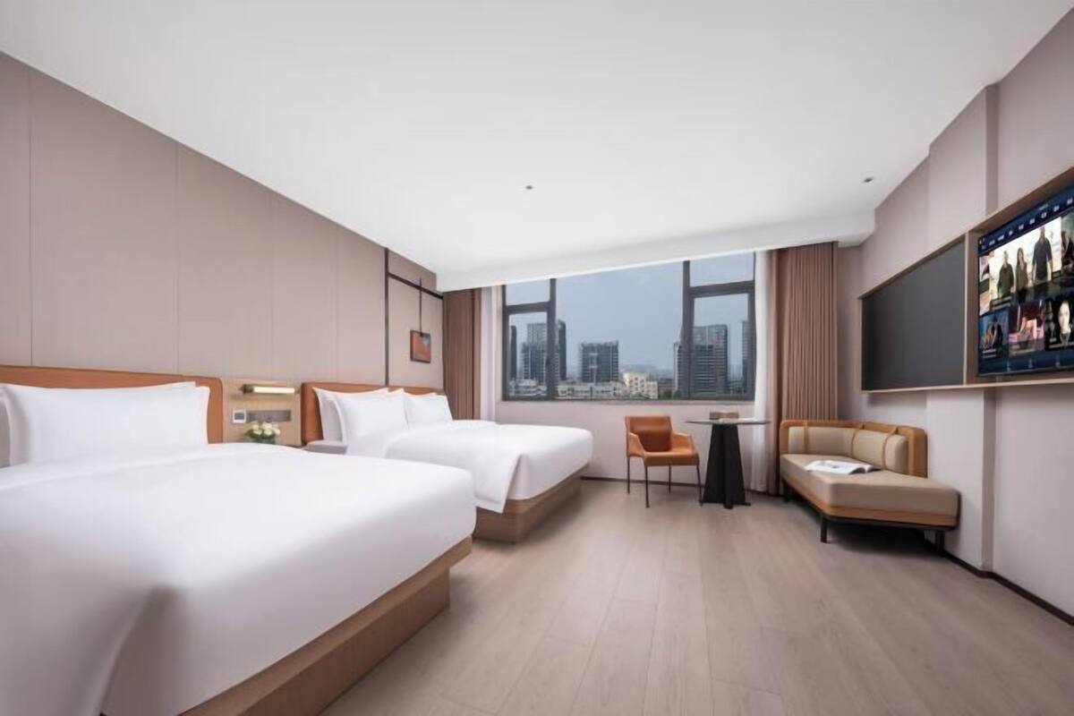Une chambre d’hôtel avec deux lits, un canapé, une télévision et une vue sur la ville.