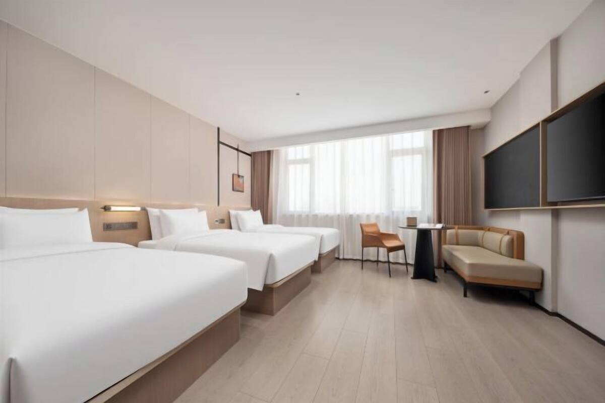 Une chambre d’hôtel avec trois lits, un canapé, une télévision et une petite table.