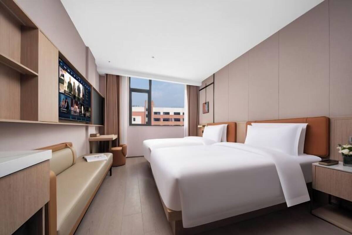 Une chambre d’hôtel avec deux lits, un coin salon, une télévision et une fenêtre donnant sur la ville.