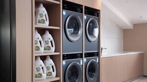 A laundry room with two stacked front-loading washing machines and shelves with detergent bottles. - Xingye International Hotel (Yiwu International Trade City) (Yiwu)