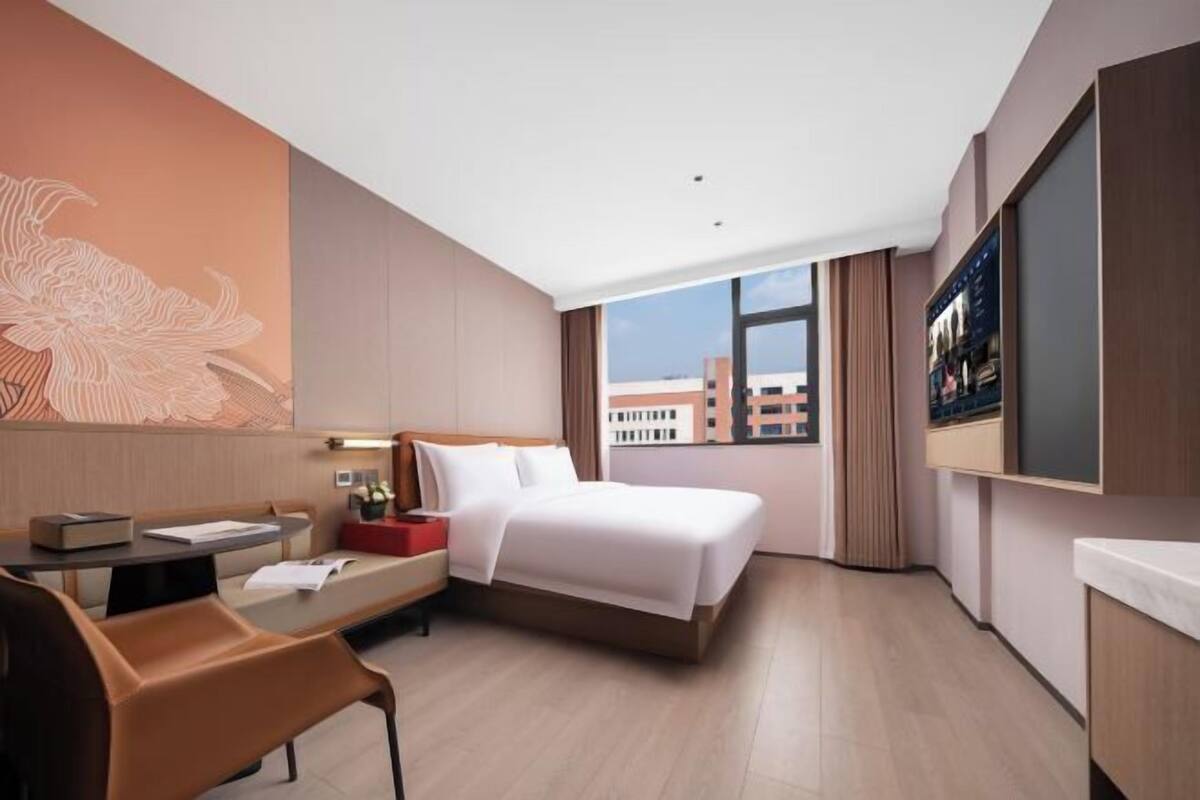Une chambre d’hôtel équipée d’un lit, d’un bureau, d’une chaise, d’une télévision et d’une grande fenêtre donnant sur la ville.