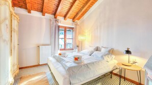A bedroom with a wooden ceiling, a bed with white linens, a small bedside table, and a radiator. - Laetitia Salo-historic Center Near Lake (Salò)