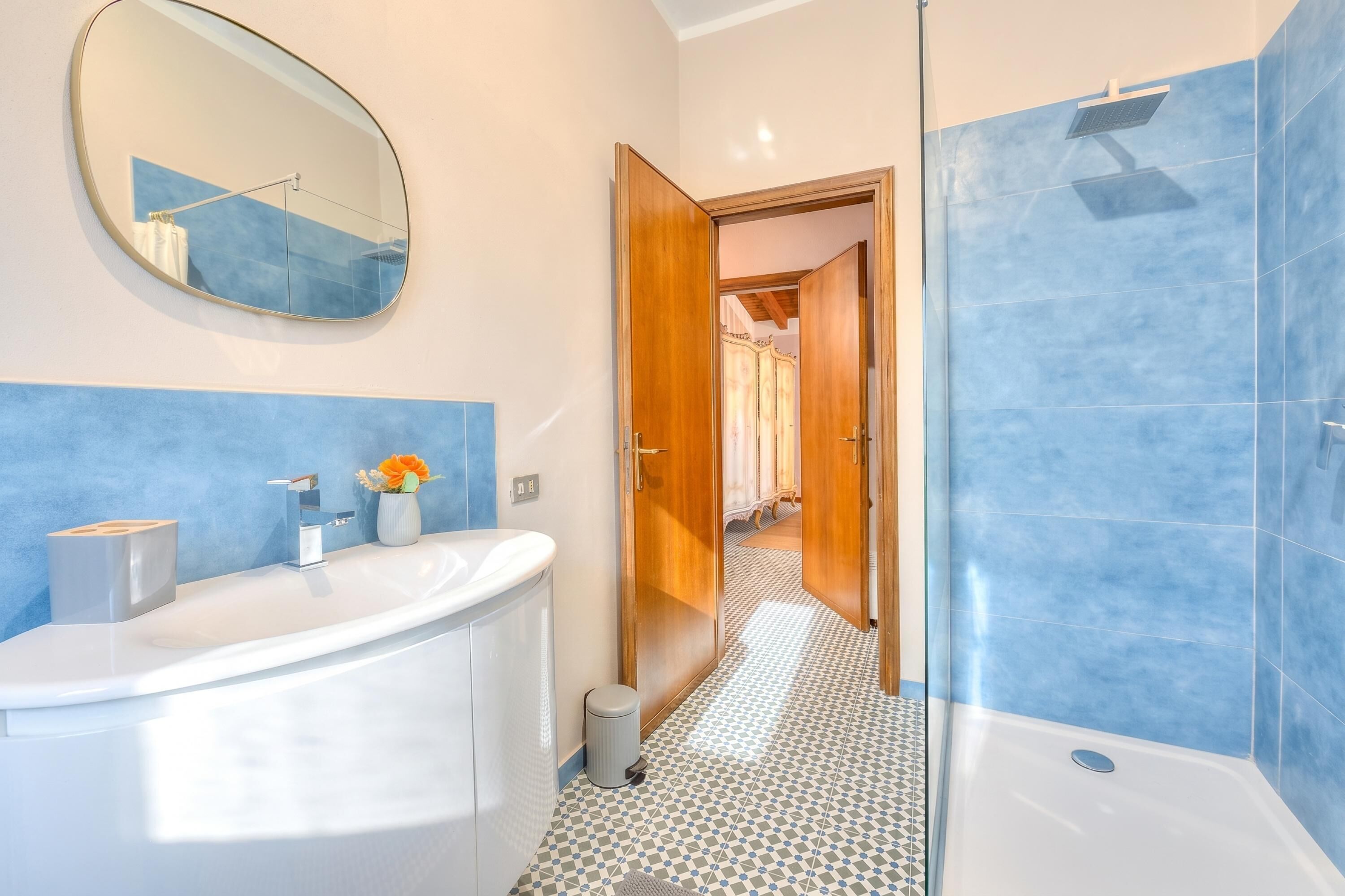 A bathroom with a white sink, mirror, and blue-tiled shower area.