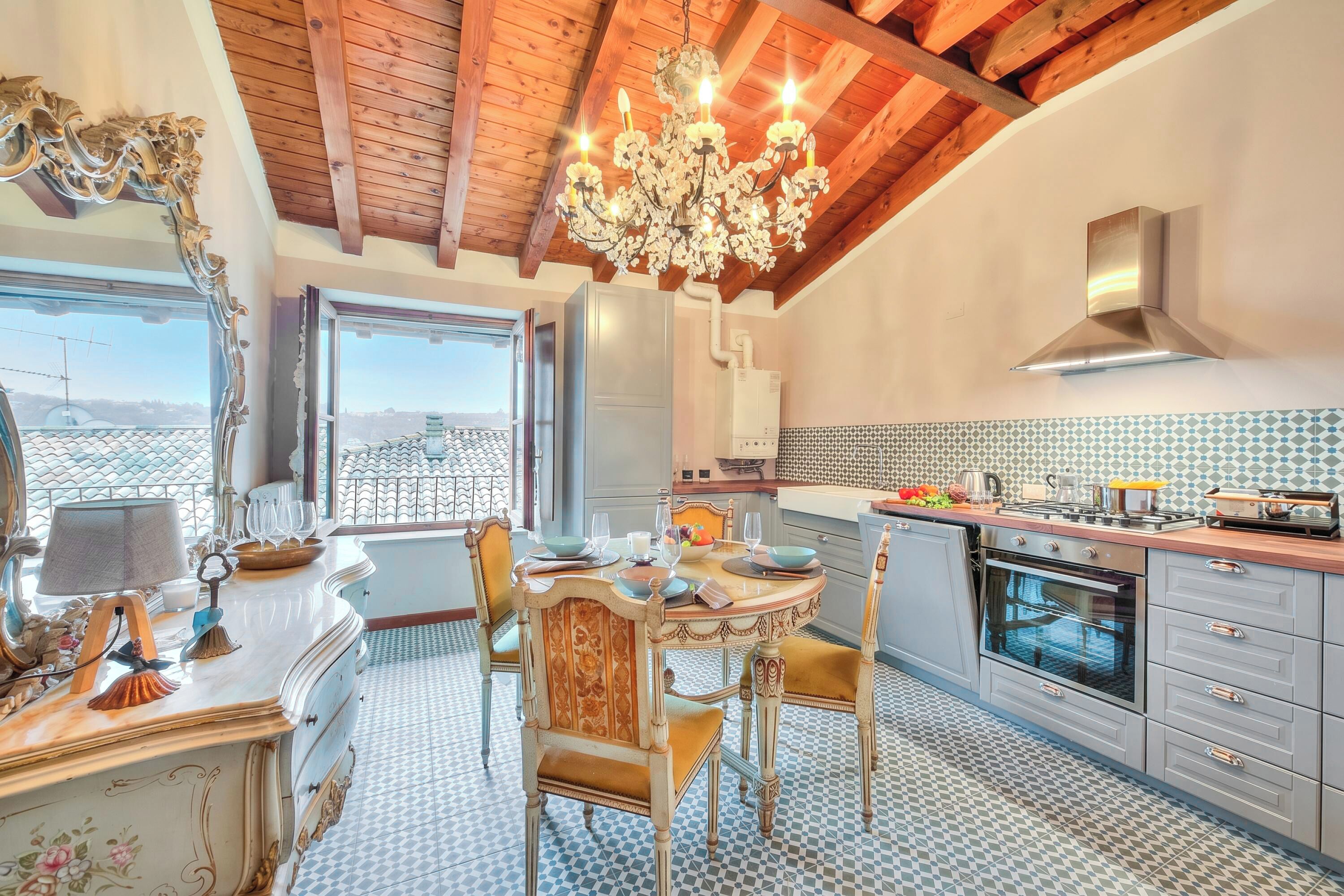 A kitchen with a chandelier, wooden ceiling beams, and a tiled backsplash.