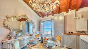 A dining area with a large ornate mirror, a chandelier, and a view of the sea through an open door. - Laetitia Salo-historic Center Near Lake (Salò)