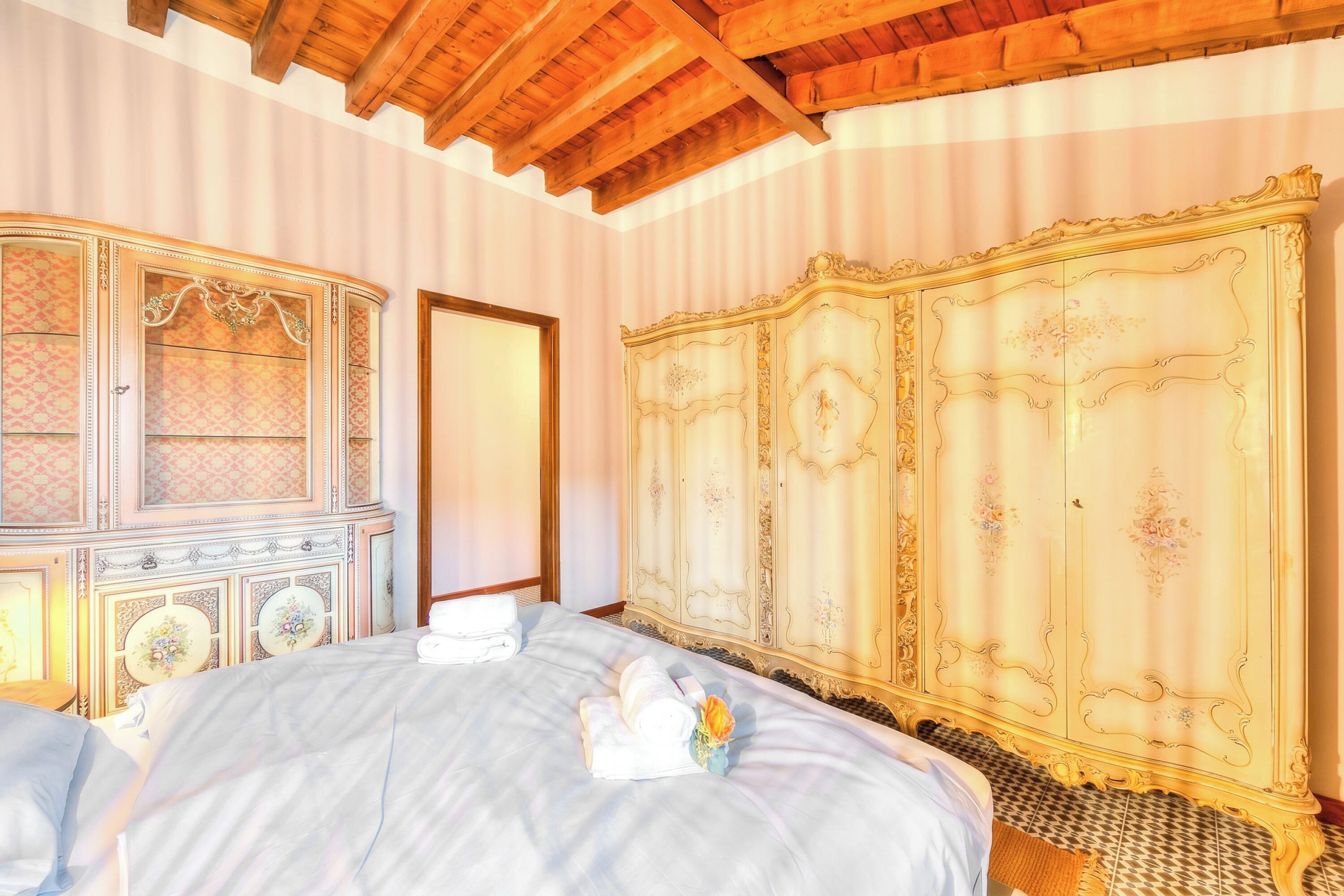 Ein Schlafzimmer mit einem Bett, einer großen, verzierten Kommode und einer Holzbalkendecke.