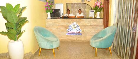 A reception area with a marble counter, two turquoise chairs, and a large potted plant.