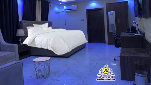 A modern hotel room with a large bed, a desk, a chair, and a small round table. - Marriot Airport Hotels (Lagos)