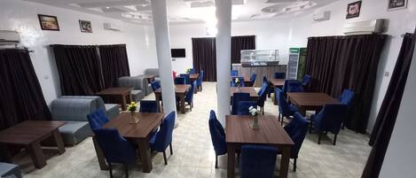 Comedor con varias mesas y sillas, unidades de aire acondicionado y una cocina al fondo.