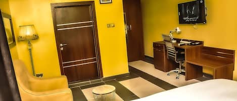 A hotel room with a bed, a desk, a chair, a TV, and a wardrobe.