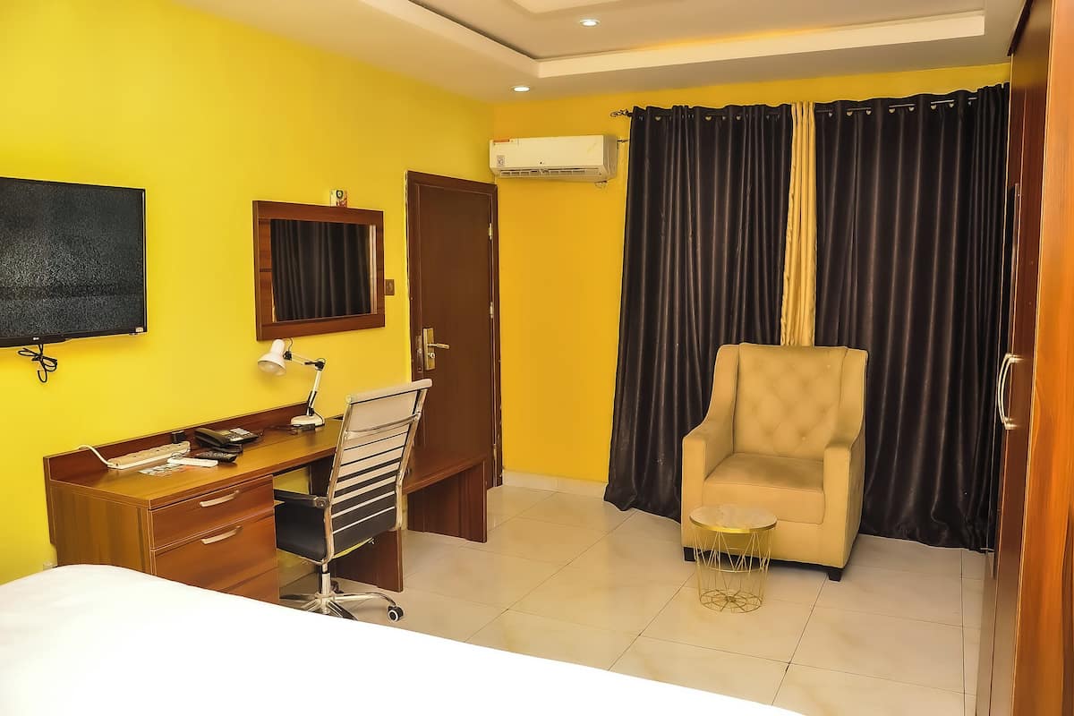 Une chambre d’hôtel avec un bureau en bois, une chaise, un lit, une télévision et une fenêtre avec des rideaux.