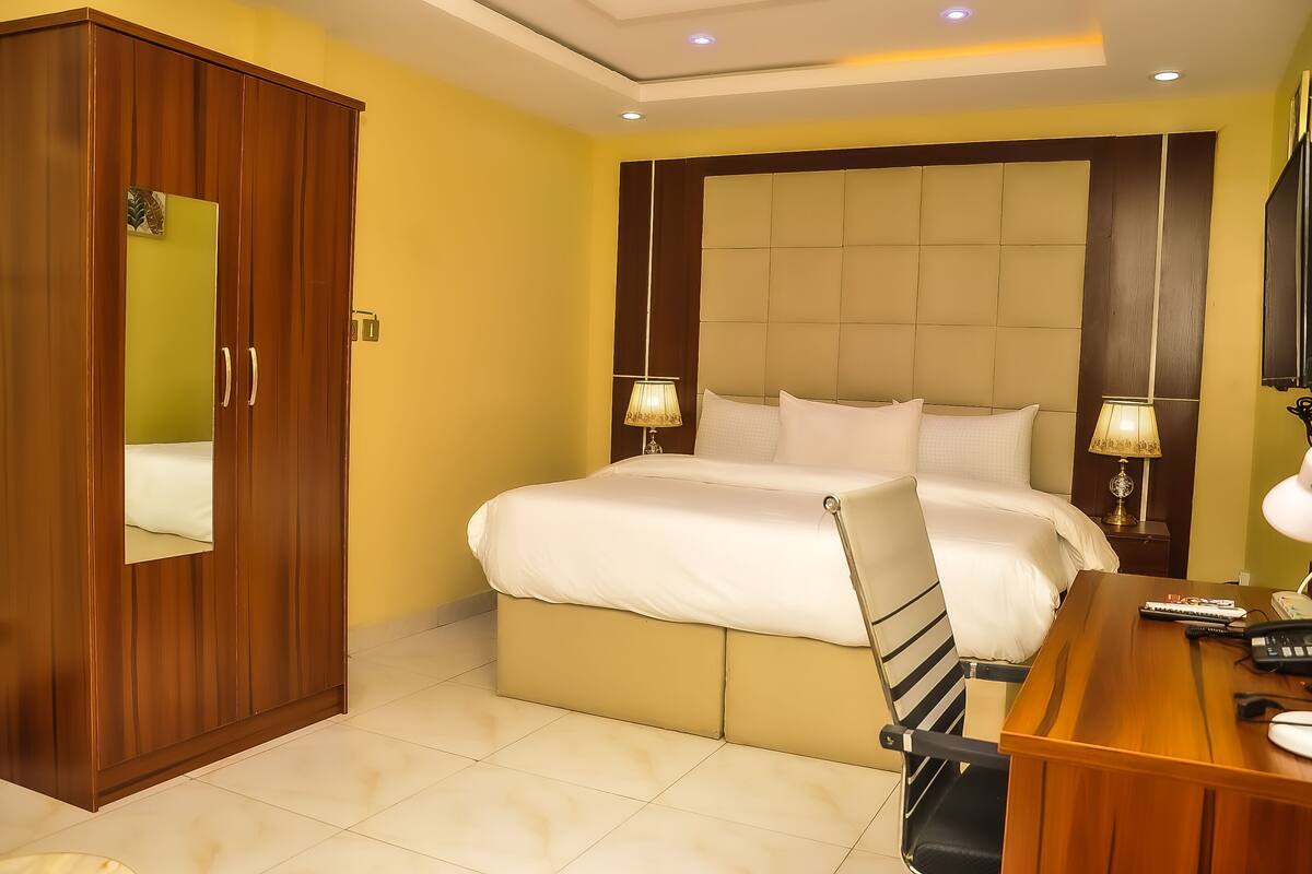 Une chambre à coucher comprenant un lit, des tables de chevet, un bureau, une armoire et un miroir.