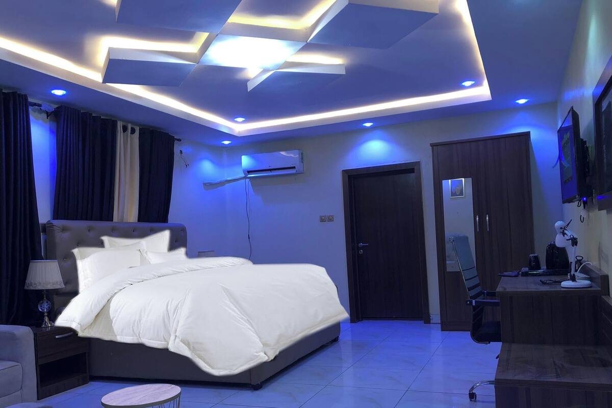 Une chambre moderne comprenant un lit, une table de chevet, une lampe, un appareil de climatisation et une armoire en bois.