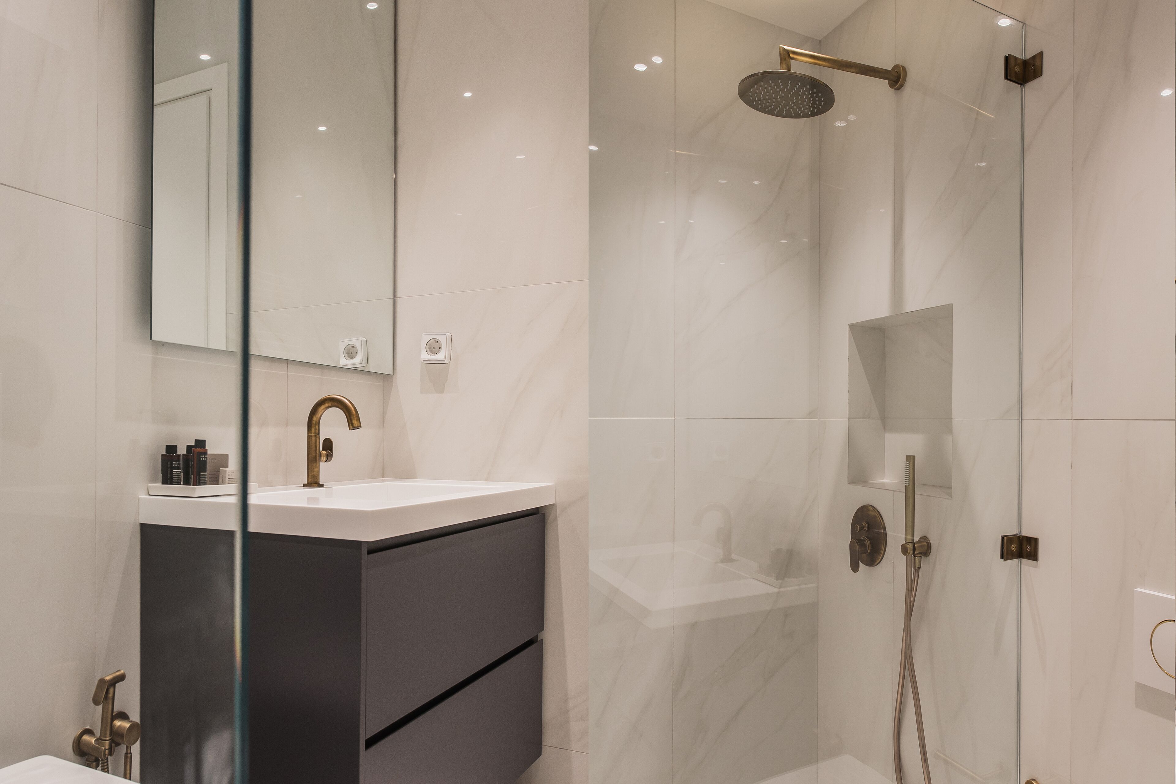 Ein modernes Badezimmer mit einer gläsernen Duschkabine, einem weißen Waschbecken und einem dunklen Schrank.