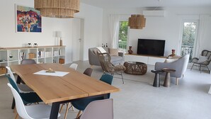 Un soggiorno moderno con un tavolo da pranzo in legno, posti a sedere confortevoli, una televisione a schermo piatto e un'ampia finestra con vista sul verde.