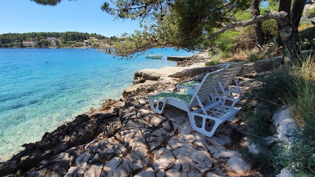 Una costa rocciosa con acque cristalline blu, una piccola barca e una sedia bianca.