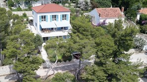 Una vista aerea di una proprietà costiera con un edificio bianco, una barca ormeggiata sulla riva e acque turchesi trasparenti.