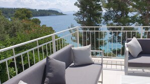 Un balcone con ringhiera bianca, due poltrone grigie imbottite e vista su un lago con una barca e colline in lontananza.