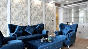 A modern living room with two blue sofas, a glass cabinet, and a patterned wall.
