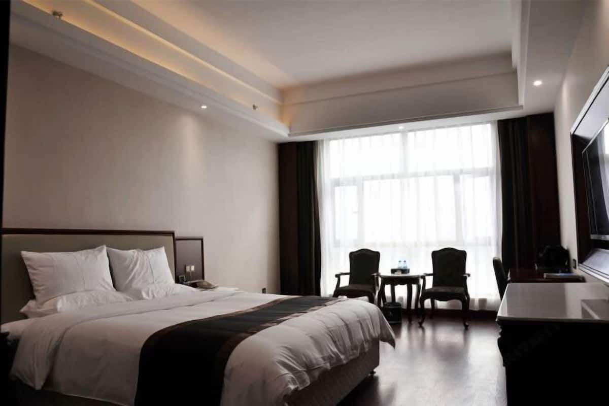Een hotelkamer met een groot bed, twee stoelen, een bureau en een televisie.