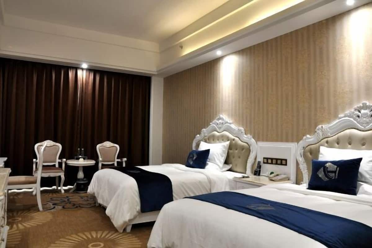 Een hotelkamer met twee bedden, een kleine tafel met stoelen en een groot raam met gordijnen.