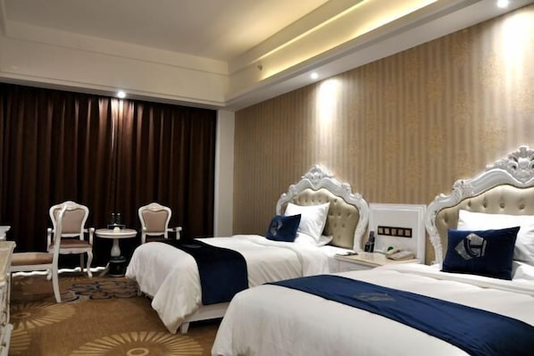 Una habitación de hotel con dos camas, una mesita con sillas y un ventanal con cortinas.