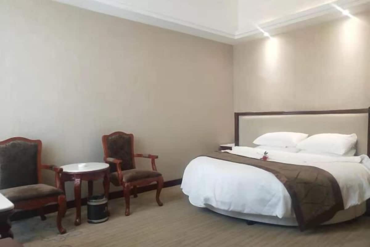 Een hotelkamer met een bed, twee stoelen, een klein tafeltje en een prullenbak.