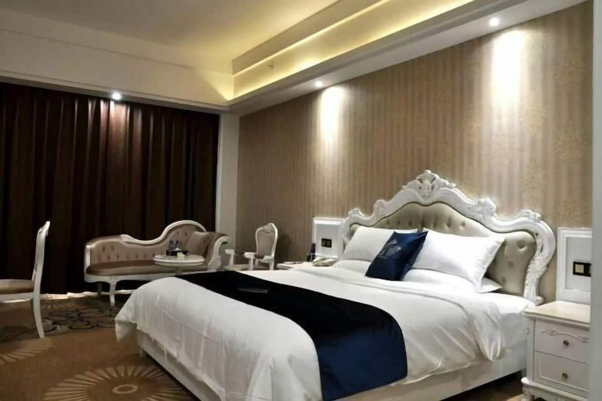 Een hotelkamer met een groot bed, een stoel, een nachtkastje en een bijzettafeltje.