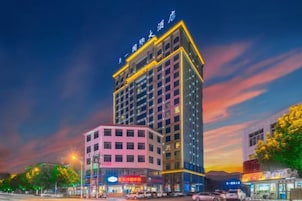 Un hotel de varios pisos con un letrero llamativo en la parte superior, varios pisos con ventanas y una zona comercial en la planta baja con tiendas.