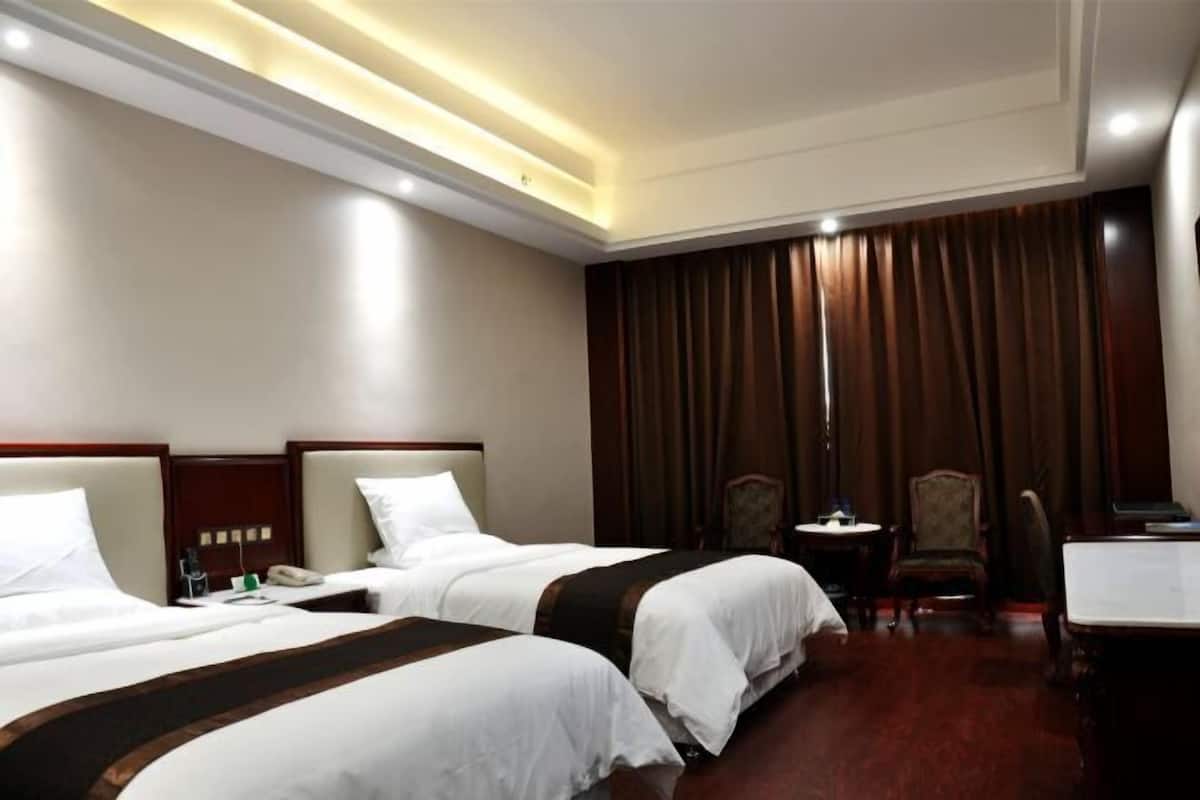 Een hotelkamer met twee bedden, een bureau, een stoel, een tafeltje en een gordijn.