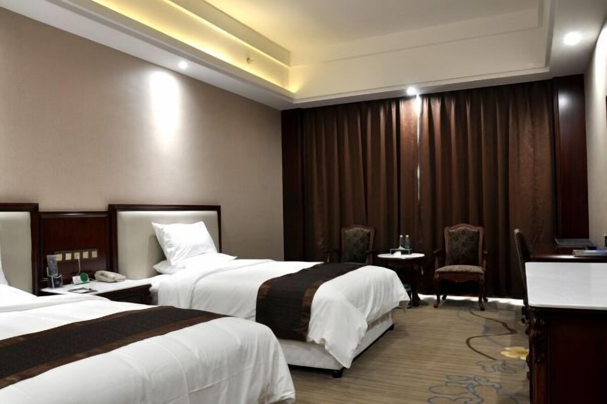A hotel room with two beds, a desk, a chair, and a large window with curtains.