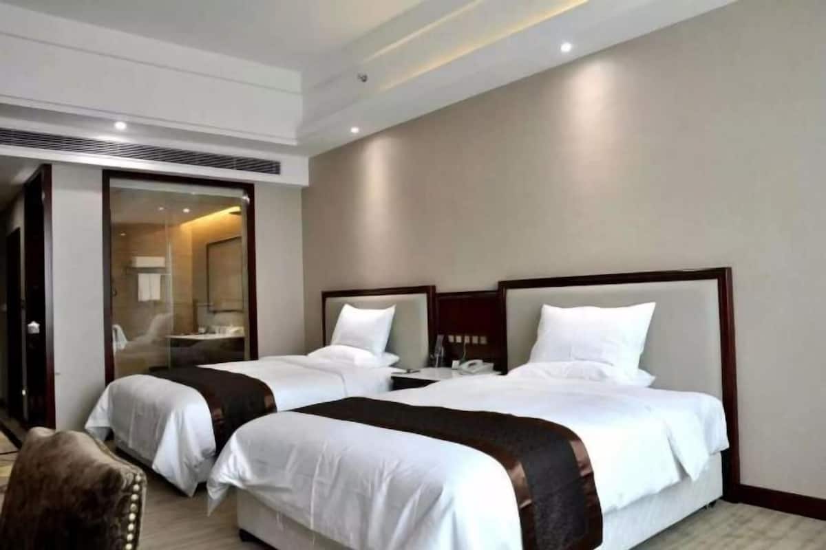 Hotelkamer met twee bedden, een grote spiegel, een houten hoofdbord en een schuifdeur naar een badkamer.
