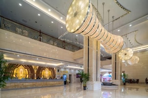 Un hall espacioso con mostrador de recepción, grandes candelabros colgantes y un techo alto.