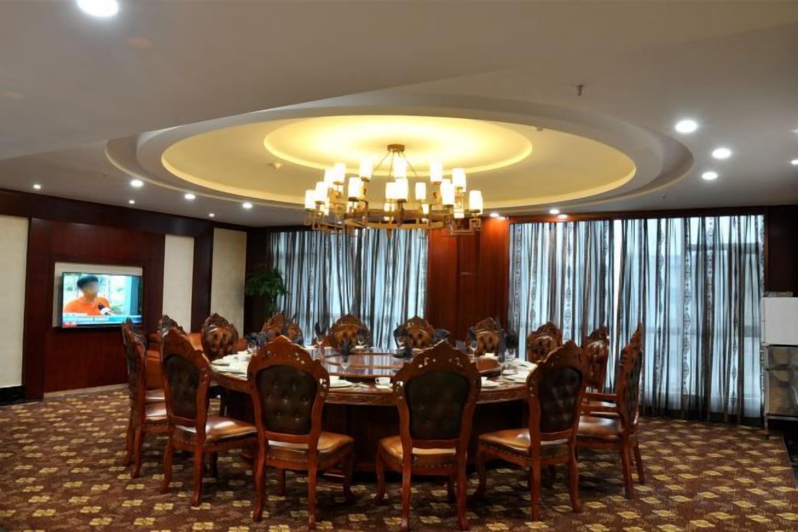A conference room with a round table, chairs, a chandelier, a television, and curtains.
