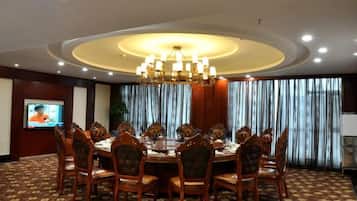 A conference room with a round table, chairs, a chandelier, a television, and curtains.