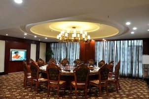 Un salón de conferencias con una mesa redonda, sillas, una araña, una televisión y cortinas.