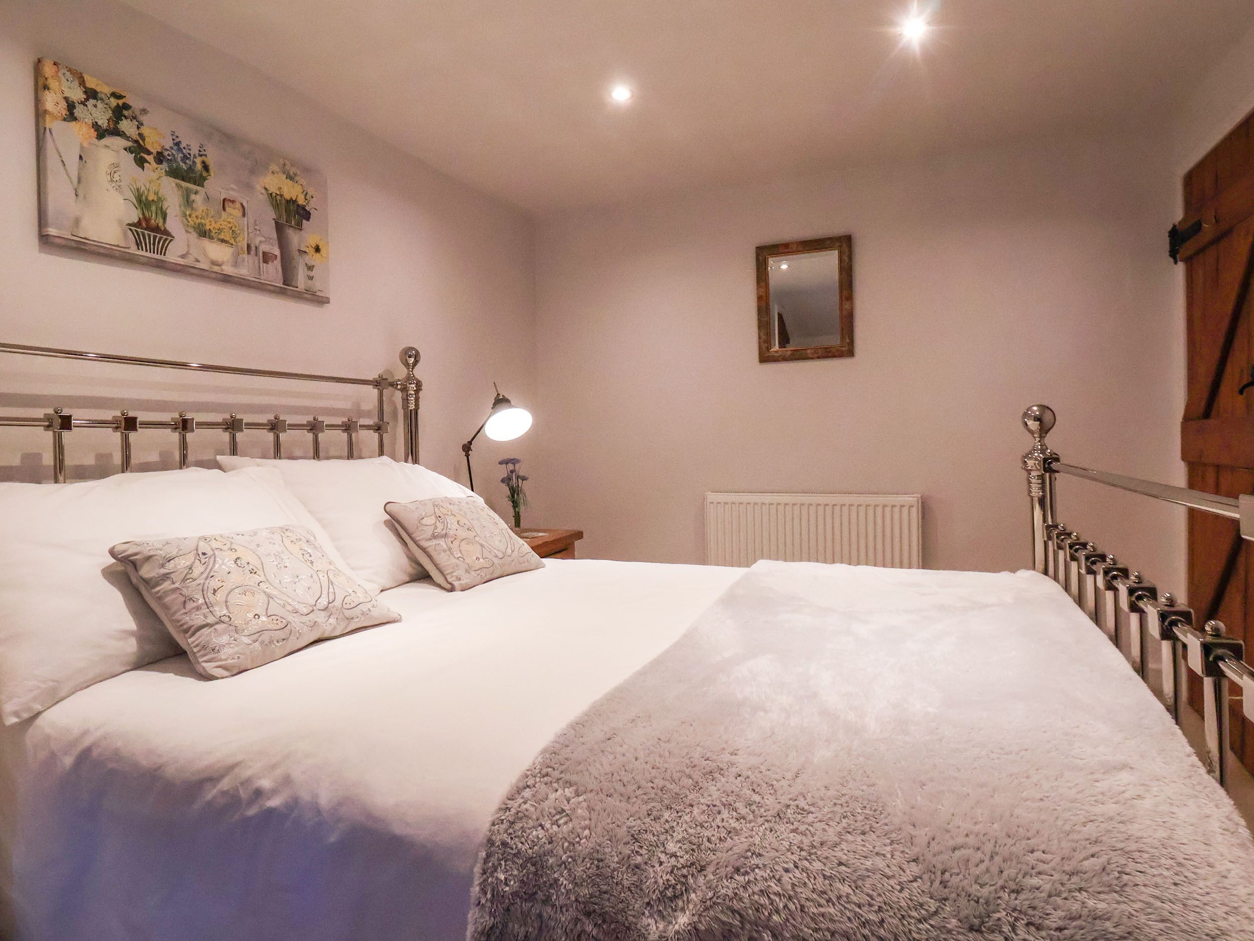 A neatly made bed with a fluffy blanket, a bedside lamp, and a floral painting on the wall.