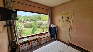 A bedroom with a large window, a bench, a bed, a TV, and a door with a towel rack. - Luxury 3 BR Villa in Marrakesh With Private Pool, Marrakesh Villa 1000 (Ourika)