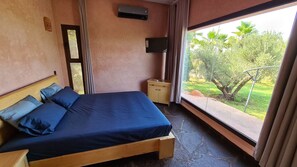 A bedroom with a bed, a nightstand, a TV, and a window with a view of greenery. - Luxury 3 BR Villa in Marrakesh With Private Pool, Marrakesh Villa 1000 (Ourika)