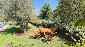 A garden with a wooden table and chairs, surrounded by greenery and flowers.