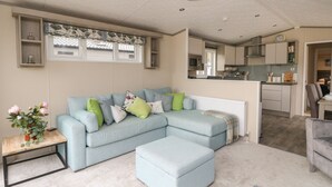 A modern living room with a sectional sofa, a small table with a vase of flowers, and a view into the kitchen.