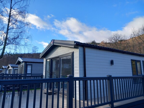 A row of modern mobile homes with large windows, a covered deck, and a mountain backdrop.