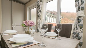 A dining table set with white plates, bowls, and glasses, a pitcher with flowers, and a view of a building through a window.