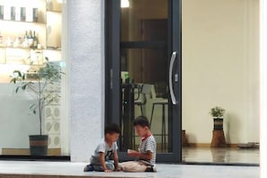 Two individuals seated on a ledge outside a building with a glass door and a potted plant nearby. - Mountain and Courtyard Homestay (Hengyang)