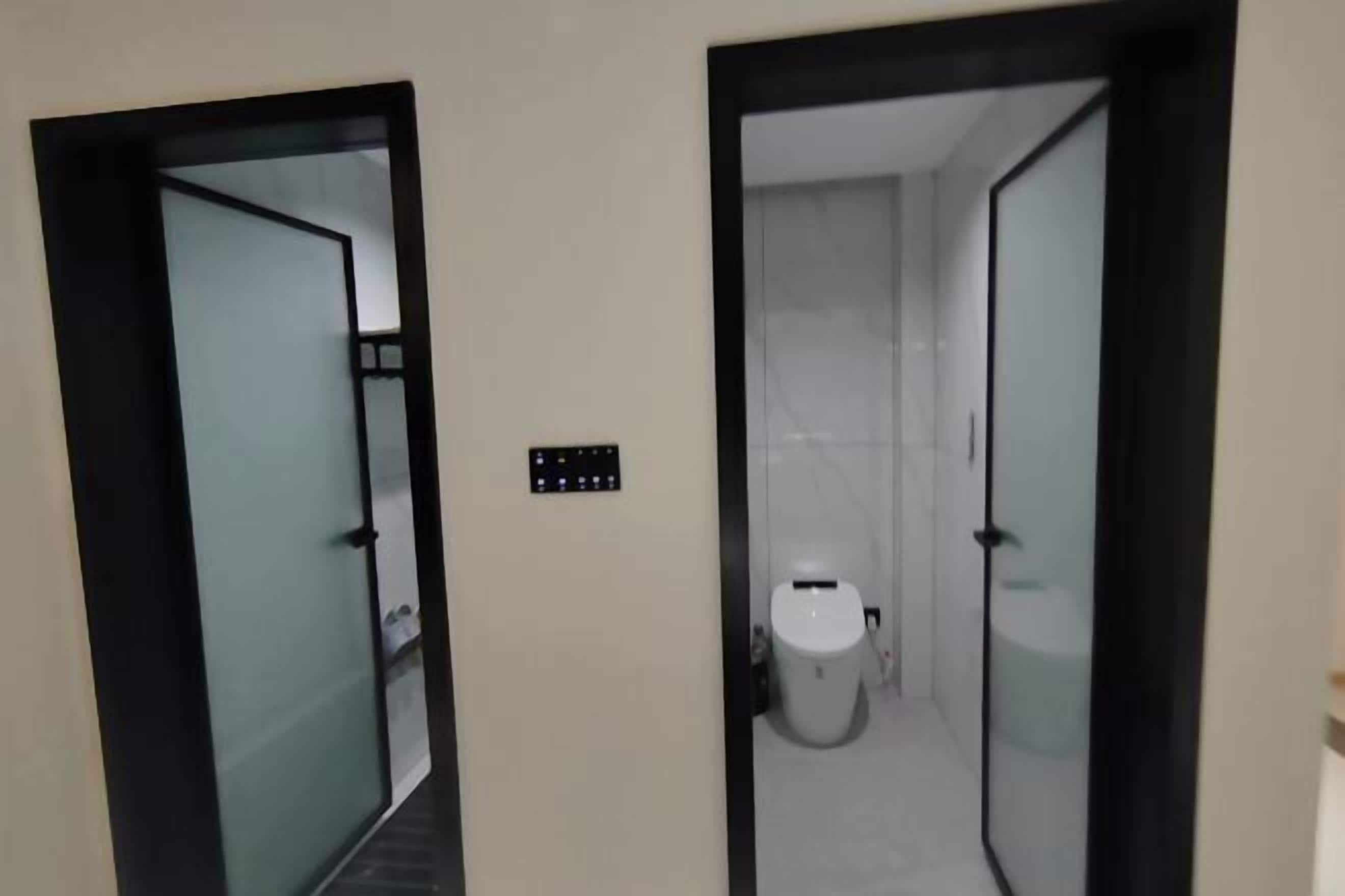 A hallway with two doors leading to a bathroom, a control panel, and a toilet.
