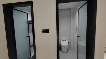 A hallway with two doors leading to a bathroom, a control panel, and a toilet.