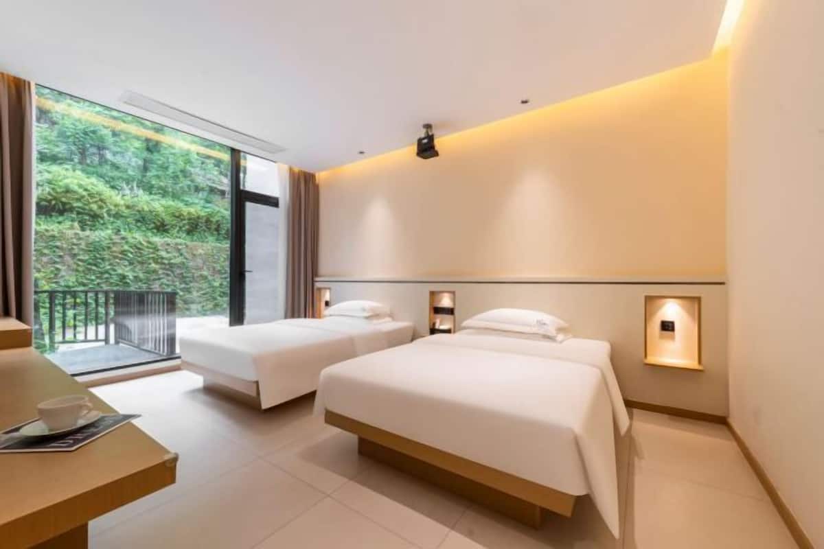 A hotel room with two beds, a balcony, and a view of greenery.