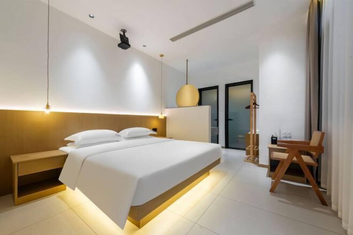 A modern hotel room with a large bed, bedside tables, a desk, and a chair.